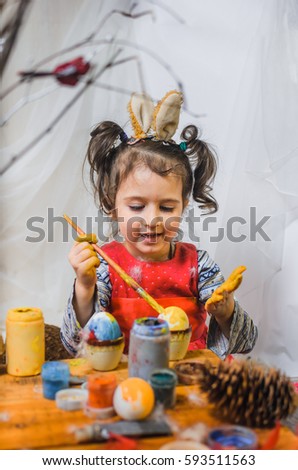 little girl 2 - 4 years in a red dress draws intently the pictures on the eggs with watercolors . at the head of the child ears of a rabbit preparing for Easter
