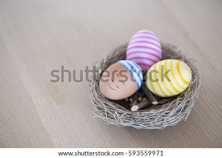 Three cheerful handmade easter eggs with handwritten smiley in straw nest, wearing dress and hat from colorful cotton, isolated on clean wooden background, free space for your text and graphics. Oak.