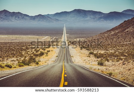 Classic vertical panorama view of an endless straight road running through the barren scenery of the American Southwest with extreme heat haze on a beautiful hot sunny day with blue sky in summer Royalty-Free Stock Photo #593588213