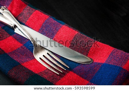 Close up of a vintage silver knife and fork on red blue napkin on a dark concrete table, horizontal image