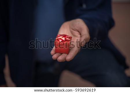Closeup of a man kneeling down and proposing, holding out a red gift box in his hand