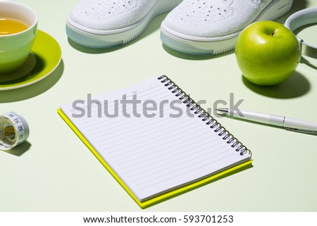 Fitness plan concept. Sneakers, tea, apple and headphone on pastel color background with open notebook.