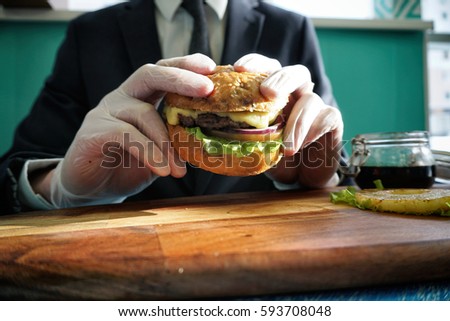 Man holding hamburger with gloves in business suit in the restaurant. Burger in hands close up.
