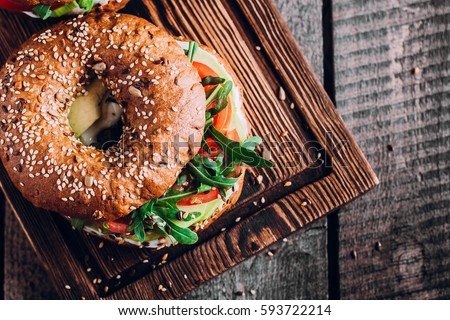 Bagels with cream, avocado, tomatos and arugula on wooden board and table background. Healthy breakfast food. Top view and Copy space Royalty-Free Stock Photo #593722214