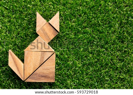Wooden tangram puzzle in cat shape on artificial green grass background