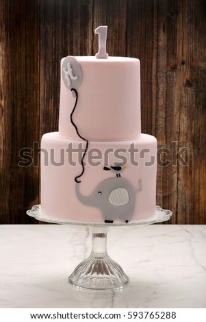 Pink birthday cake with elephant on wooden background and place for text
