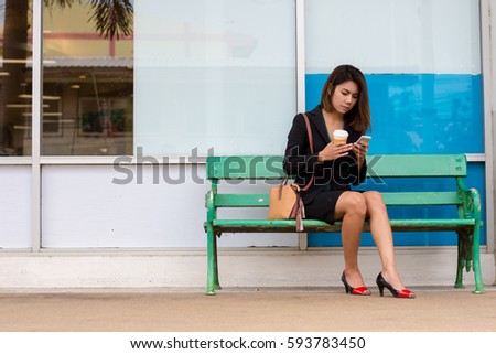 Business women are playing mobile phone, sitting on a bench in the city.