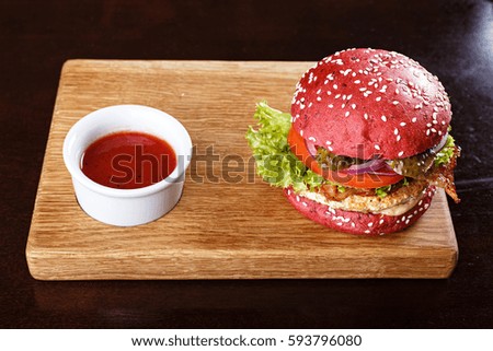Red burger with cutlet, bacon and vegetables, sprinkled with sesame seeds on a blackboard. Horizontal photo with free space area for text or design.