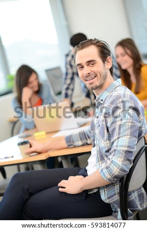 portrait of a young man in casual wear working in creative business startup company office with coworker people in background 