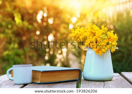 old book, cup of coffee next to field flowers on wooden table outdoors at afternoon. selective focus