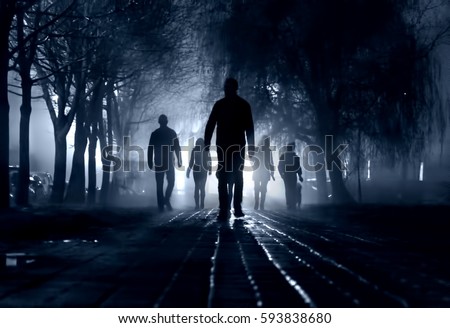 Silhouettes of people zombie walk at night in the city in the moonlight in the soft blurred focus on a dark blue background. Artistic image of a zombie people. Royalty-Free Stock Photo #593838680
