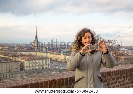 beautiful girl taking picture with smartphone with panoramic view of Turin cityscape and Mole Antonelliana