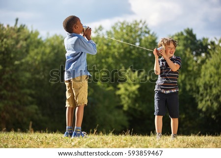 Two boys playing tin can telephone at the park Royalty-Free Stock Photo #593859467