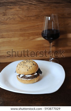 Burger and a glass of red wine on a wooden background. Free space for design. White plate