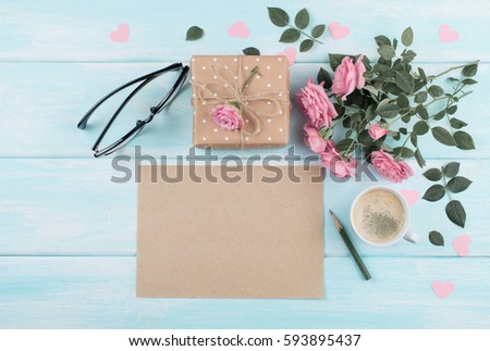 Pink roses with blank sheet paper for greeting text and gift box, coffee cup on background of shabby wooden planks. Copy space. Top view. Flat design.