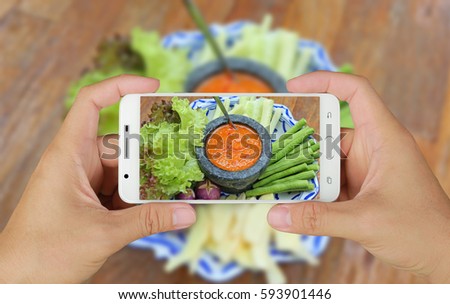 Hands taking picture of chilli crab egg with vegetables with smartphone.