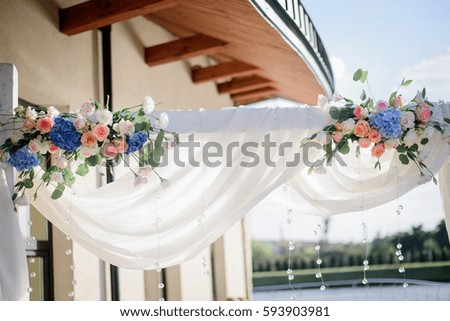 Bouquets of white roses and blue hydrangeas hang on wedding altar outside