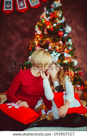 Mother and daughter hold red pillows sitting before Christmas tree