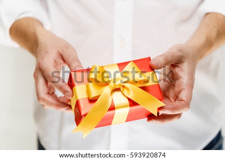 Male hands holding a gift box. Present wrapped with ribbon and bow. Christmas or birthday red package. Man in white shirt.