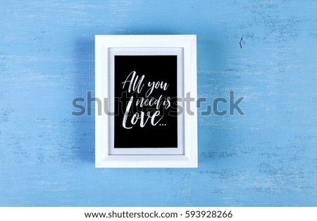 Blank photo frame on blue wood background. All you need is love text. Painted scraped wooden board. Grunge plywood texture or pattern.