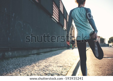 Athlete woman preparing for running on the city street. Legs warming and stretching. Sport tight clothes. Blurry background. Horizontal Royalty-Free Stock Photo #593935241