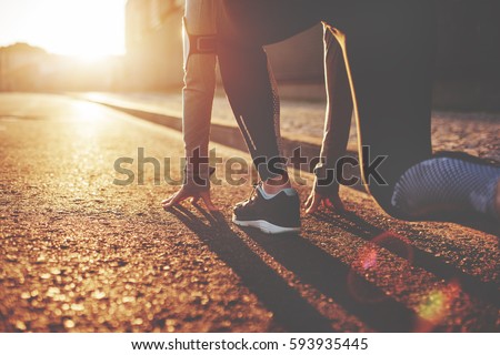Athlete woman in running start pose on the city street. Sport tight clothes. Bright sunset, blurry background. Horizontal Royalty-Free Stock Photo #593935445