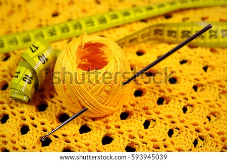 A metal hook for hand-knitting is stuck in a tangle of yellow yarn and a stripe lies on the finished product with a pattern