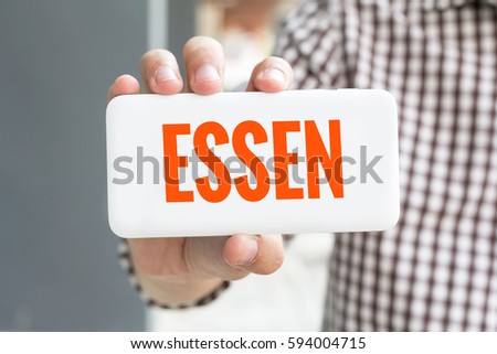 Man hand showing ESSEN word phone with  blur business man wearing plaid shirt.