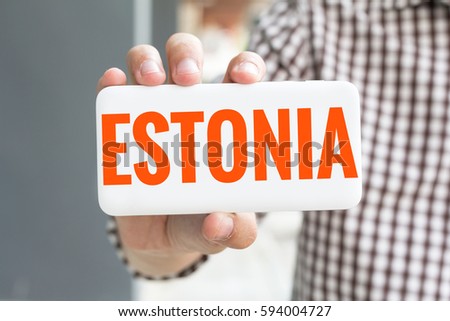 Man hand showing ESTONIA word phone with  blur business man wearing plaid shirt.