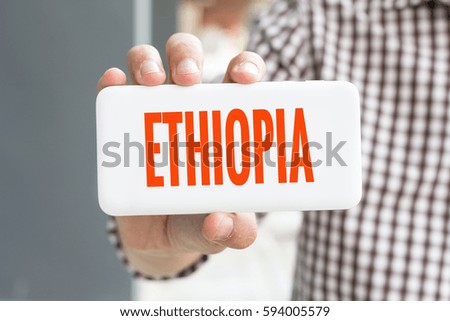 Man hand showing ETHIOPIA word phone with  blur business man wearing plaid shirt.
