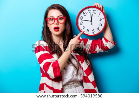 beautiful surprised young woman with clock standing in front of wonderful blue background