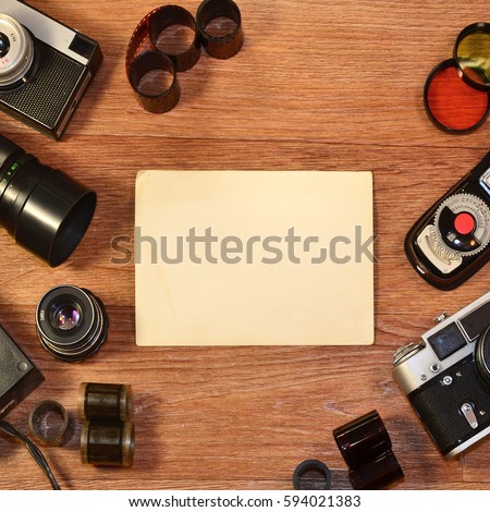 Retro camera and some old photos on wooden table. Vintage mock up for artwork or logo design presentation with film camera and lens. View from above