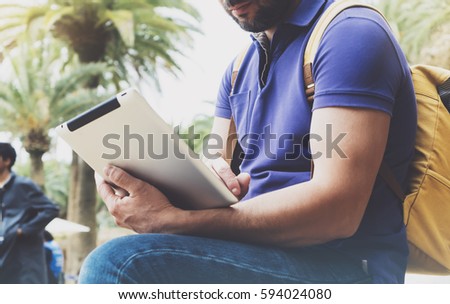 Hipster person holding in hands digital tablet with blank screen, man reading on computer on background nature park palm landscape, mock up technology blur, male hands tourist using gadget, smile