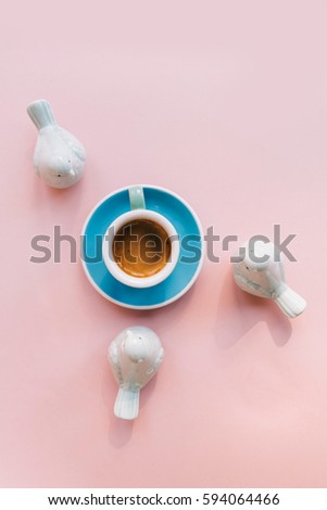 Freshly brewed morning cup of espresso coffee with a beautiful crema on the pink background with green ceramic birds decorating the flat lay