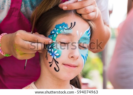 Child animator, artist's hand draws face art to little girl. Blue butterfly painting. Children birthday party entertainment