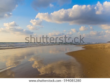 The sea rolls on a sandy beach, sky reflection. Royalty-Free Stock Photo #594085280
