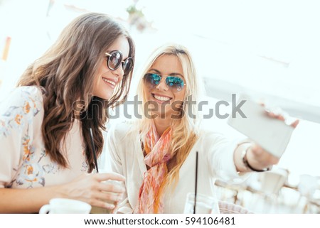 Two young women drinking coffee and using smart phone in cafe.