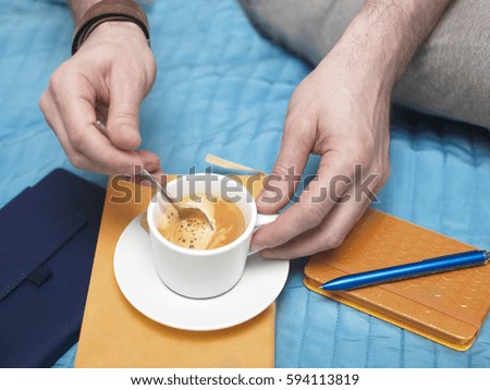 Man sitting on a bed with a cup of espresso and a day planner, closeup cropped shot