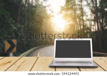 Laptop with blank screen on wooden table with dark misty forest, road and flare light background, can used for display or montage your products
