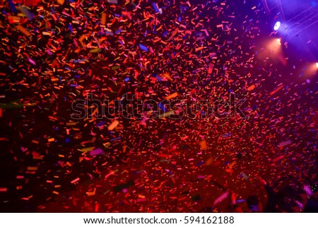 Confetti fired on air during a concert. People are happy and with hands in the air. Image ideal for backgrounds. Red are the tones of the picture