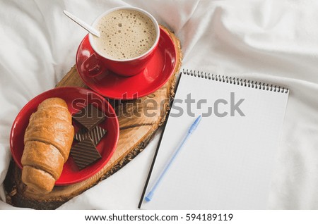 Cup of Hot Cappuccino Croissant and Chocolate in the Bed, Empty Notebook for Note. Selective Focus. Copy space.