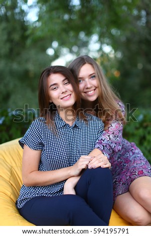 Portrait of two smiling lovely young women of European appearance posing for photo shoot or advertising of cosmetics or clothing catalogs. Women's successful students came to park after school to