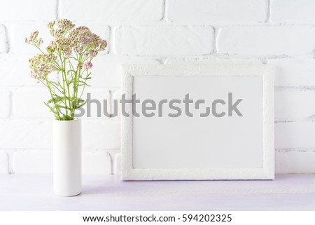 White landscape frame mockup with creamy pink flowers in cylinder vase near painted brick wall. Empty frame mock up for presentation design.  Template framing for modern art.
