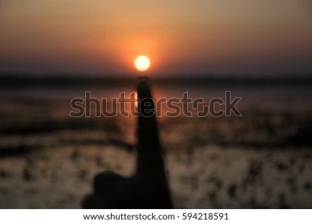 children show your hand  and point to the sun,with sunset background, blur image