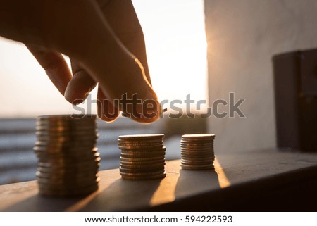man hand place coin on coin stack against the sun siluate. money save concept.