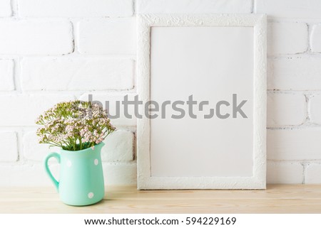 White frame mockup with wild very soft pink flowers in mint pitcher near painted brick wall. Empty frame mock up for presentation design.  Template framing for modern art.