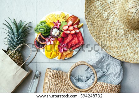 Fresh fruit plate and set of summer fashion beach accessories, top view from above (overhead). Tropical beach lifestyle. Royalty-Free Stock Photo #594248732