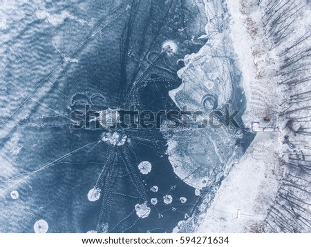Flight over frozen lake breaking ice in rural village, Lithuania. Aerial photography during winter season.