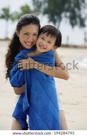 Mother hugging son on beach, son wrapped in blue towel