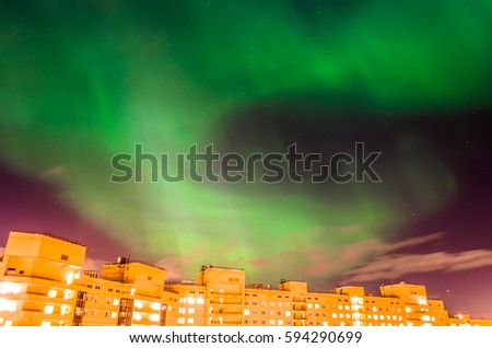Aurora borealis green starry night over the city and houses.